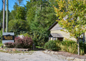 black rock granite &amp; cabinetry sign stands amidst lush greenery beside a building. the sign, with its black background and bold yellow text, contrasts with the natural landscape. a gravel driveway leads to the building.